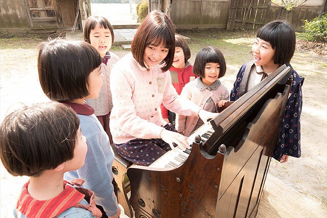 woman playing an organ with children around her