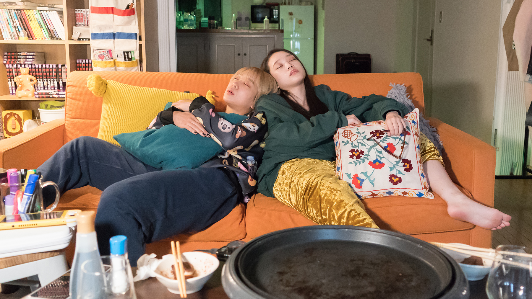 two kids napping on a couch in a messy apartment
