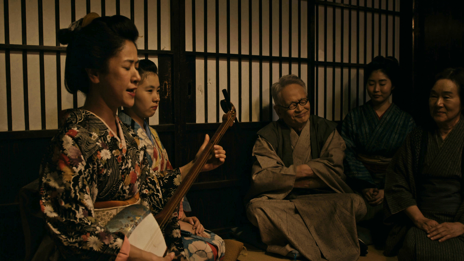 group of people surrounding woman with shamisen
