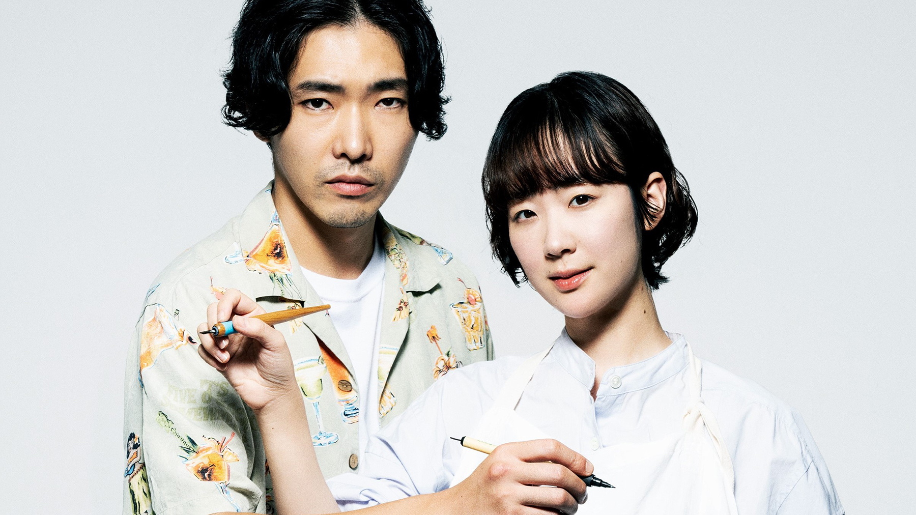 man and woman standing next to each other, each holding a pen